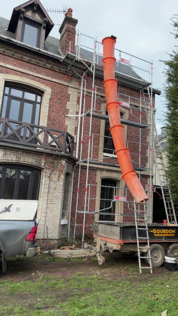 Rénovation de toiture en cours avec échafaudage et goulotte d'évacuation sur maison briques en Seine-Maritime