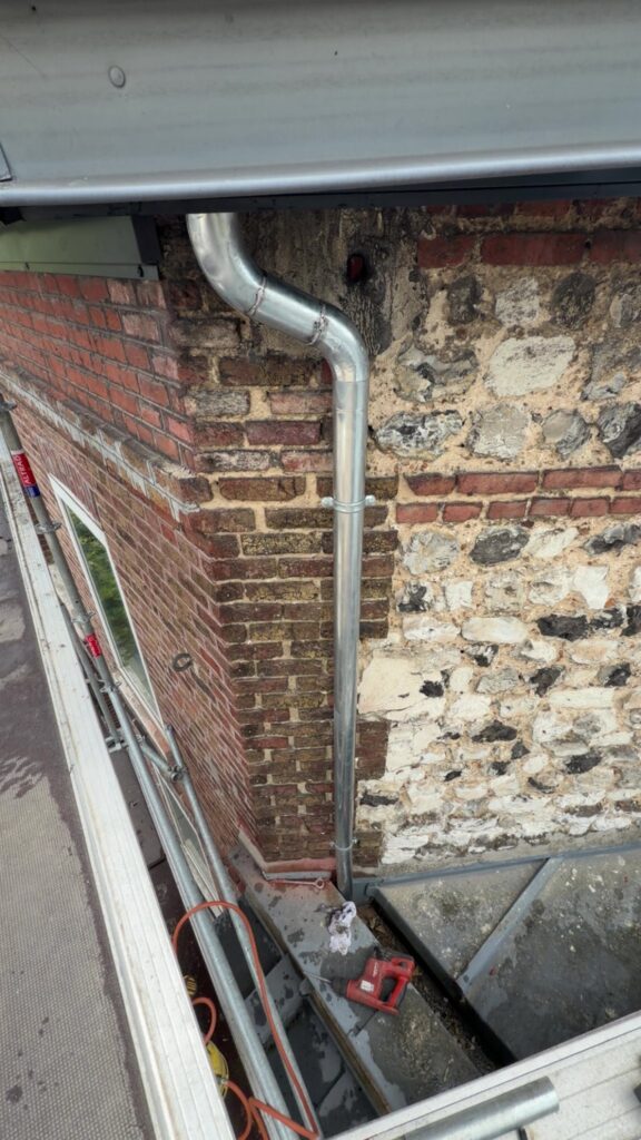 Pose d'une descente de gouttière en inox sur un mur ancien en briques et silex par Houisse Couverture